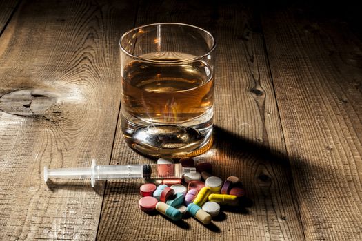 Alcohol, pills and syringe on table with shadow