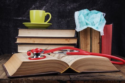 Stethoscope on open book and coffee on books pile