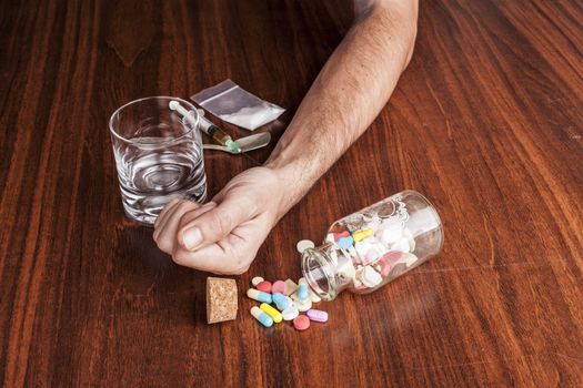 Pills and drugs with empty glass and hand on brown wood table