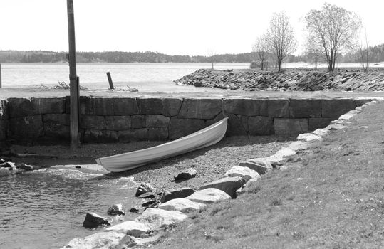 Small white rowboat on a small stony area of shore, against a stone wall on Suomenlinna island, Finland - monochrome processing