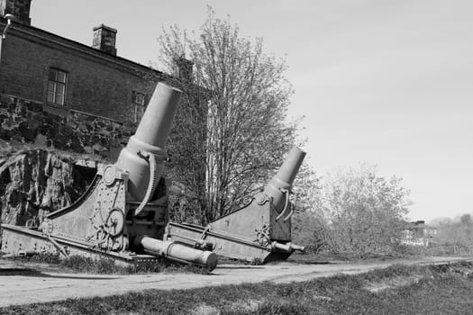 Two rusted cannons in front of a military building on Suomenlinna island, Finland. A total of 100 stand on the sea fortress - monochrome processing