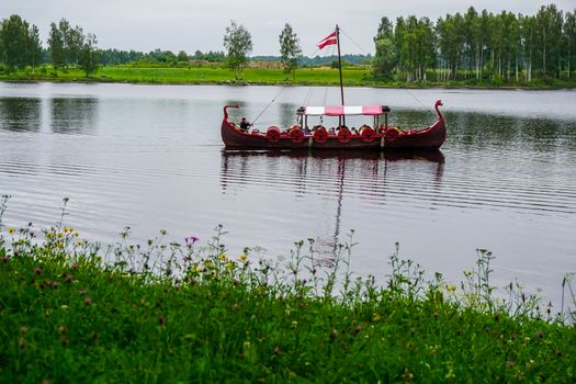 Tourist boat in the style of viking on river Daugava, Latvia. Ancient boat in Daugava river at Koknese. Old wooden viking boat in river Daugava, Latvia.