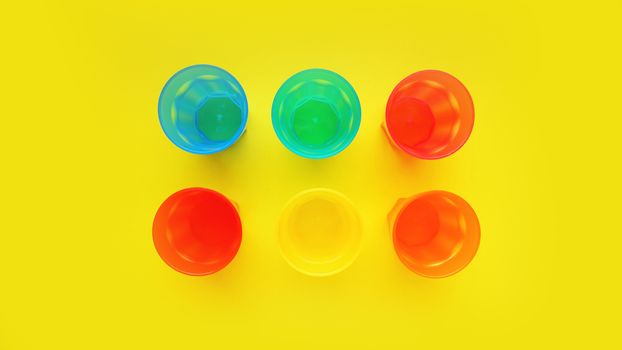 Plastic glass of various color isolated on yellow background - bright summer concept for design and banners
