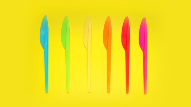 Plastic knives violet, orange, yellow, blue, red isolated on yellow background - bright summer concept for design and banners