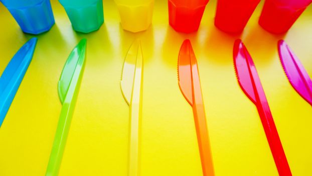 Colored plastic ware. Tableware for a picnic made of colored plastic. Knives and mug in the set of crockery for picnics, tourism and any travel. Yellow background - bright summer concept