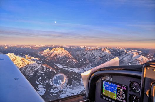Light Sport Aircraft flying above Alpine peaks over Austria in sunset, flying above the Alps, travel and landscape concept, winter tourism in Europe