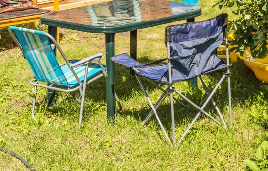 Plastic folding table and folding chairs for camping stand on the grass on a Sunny summer day.