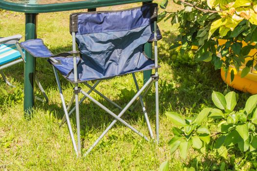 Plastic folding table and folding chairs for camping stand on the grass on a Sunny summer day.