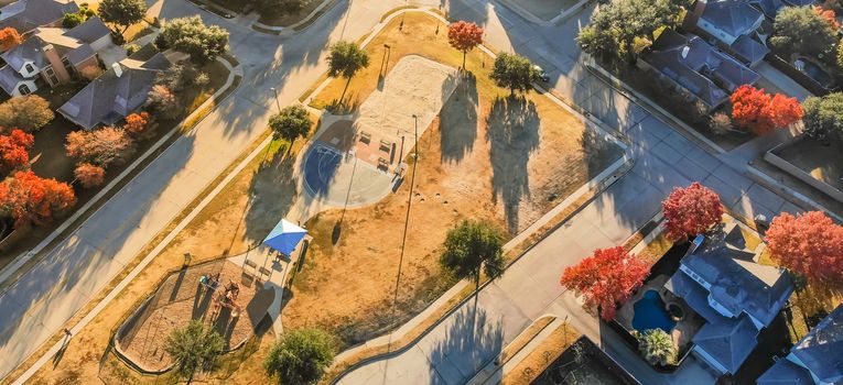 Panorama aerial view of small playground with structure and sand ground in residential area near Dallas, Texas, USA. Single-family houses with bright colorful fall foliage leaves