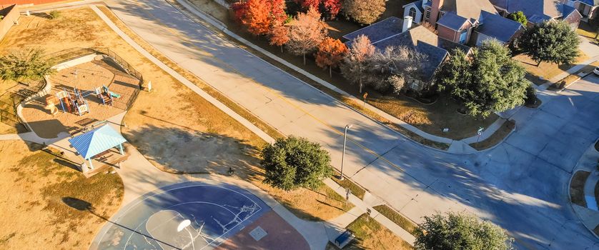 Panorama aerial view of small playground with structure and sand ground in residential area near Dallas, Texas, USA. Single-family houses with bright colorful fall foliage leaves