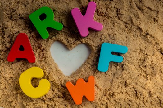 Heart shape and colorful Letters made of wood on sand