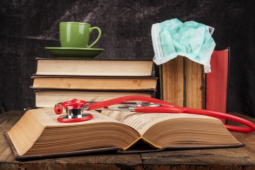 Stethoscope on open book and coffee on books pile