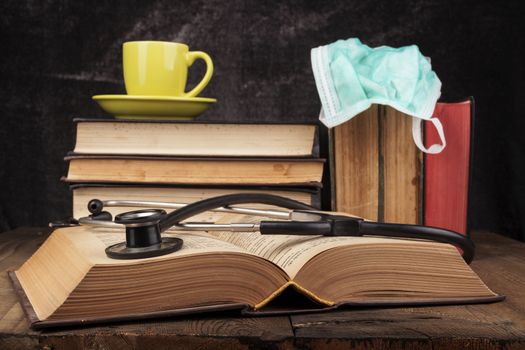 Stethoscope on open book and coffee on books pile