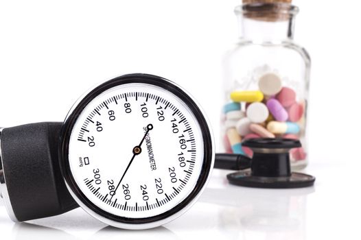 Blood pressure sphygmomanometer close-up with stethoscope and pills in the background