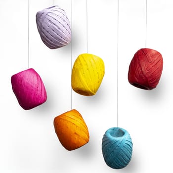 some colored raffia balls hanging from a white surface