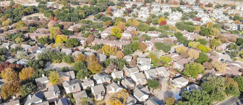 Panorama aerial drone view urban sprawl in suburban Dallas, Texas during fall season with colorful leaves. Flyover subdivision with row of single-family detached houses and apartment complex