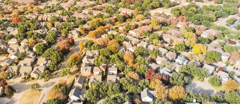 Panorama aerial drone view urban sprawl in suburban Dallas, Texas during fall season with colorful leaves. Flyover subdivision with row of single-family detached houses and apartment complex