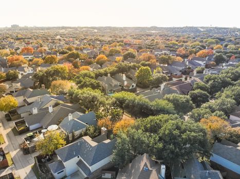 Aerial drone view urban sprawl in suburban Dallas, Texas during fall season with colorful leaves. Flyover subdivision with row of single-family detached houses and apartment complex