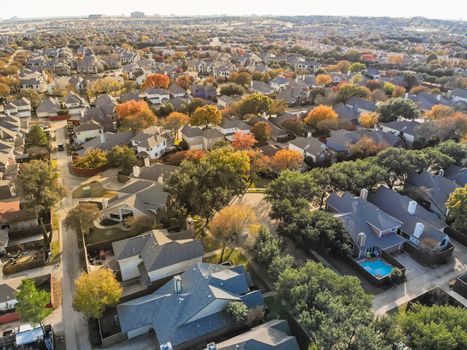 Aerial drone view urban sprawl in suburban Dallas, Texas during fall season with colorful leaves. Flyover subdivision with row of single-family detached houses and apartment complex