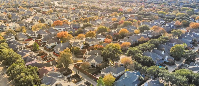 Panorama aerial drone view urban sprawl in suburban Dallas, Texas during fall season with colorful leaves. Flyover subdivision with row of single-family detached houses and apartment complex