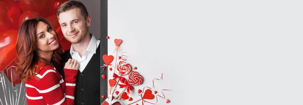 Beautiful couple with valentines day decor of red hearts , ribbons, lollipops and strawberries , white copy space for text