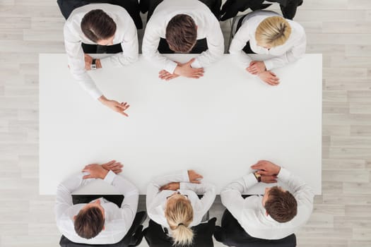 Business people sitting around empty table , copy space for text , business man pointing to blank copy space in the middle