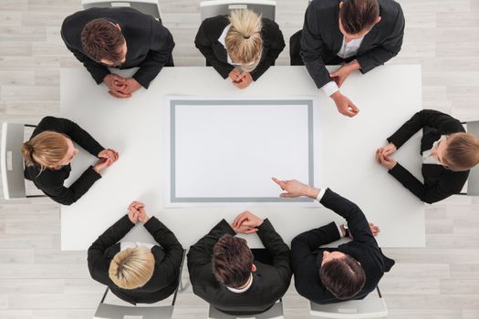 Business people sitting around empty table , copy space for text , business man pointing to blank copy space in the middle