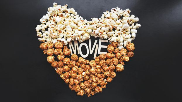 Popcorn on black background. Watching a movie with popcorn. Copy space. Pop corn. Top view. Flat lay. Wooden letters movie with hearts