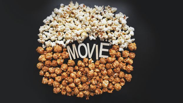 Popcorn on black background. Watching a movie with popcorn. Copy space. Pop corn. Top view. Flat lay. Wooden letters movie