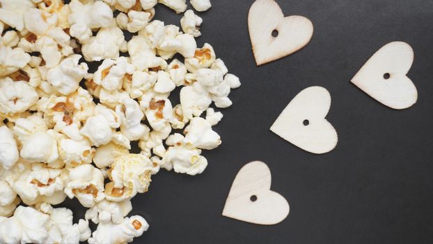 Love popcorn concept. Horizontal photo. Sweet food. Classic salted popcorn with wooden hearts on a black background