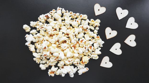 Love popcorn concept. Horizontal photo. Sweet food. Classic salted popcorn with wooden hearts on a black background