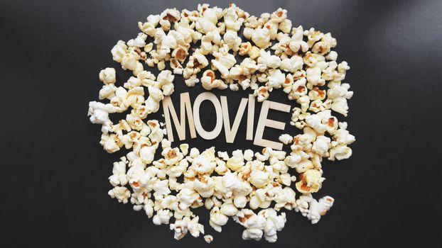 Popcorn on black background. Watching a movie with popcorn. Copy space. Pop corn. Top view. Flat lay. Wooden letters movie