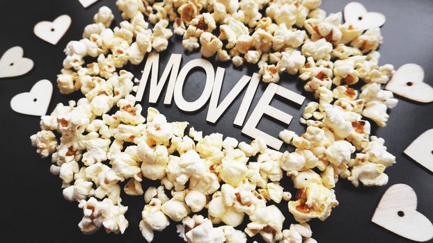 Popcorn on black background. Watching a movie with popcorn. Copy space. Pop corn. Top view. Flat lay. Wooden letters movie with hearts