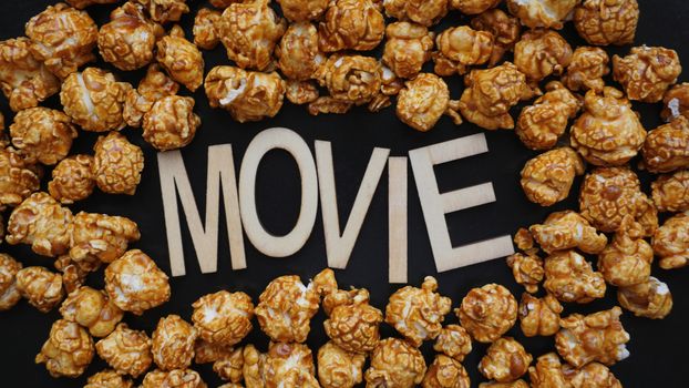 Golden caramel popcorn closeup. Background of popcorn. Snacks and food for a movie. Wooden letters Movie on a black background