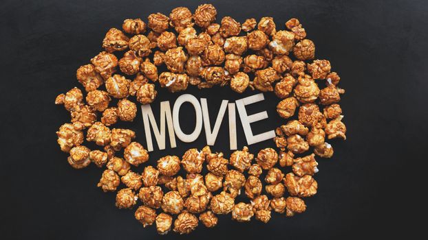 Golden caramel popcorn closeup. Background of popcorn. Snacks and food for a movie. Wooden letters Movie on a black background