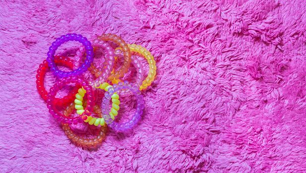 many plastic hair cable elastics in diverse colors isolated on a soft pink background