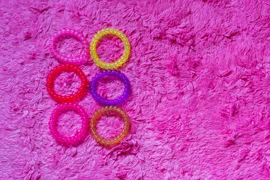 bunch of plastic cable hair elastics in different colors isolated on a soft pink background, girl hair accessories