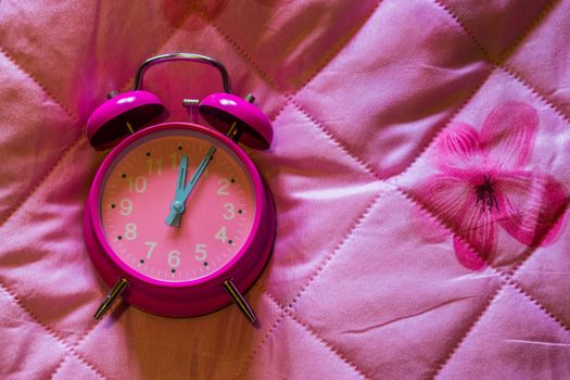 pink girly vintage alarm clock isolated on a pink blanket background