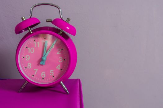 pink vintage alarm clock standing on a table with a purple wall in the background