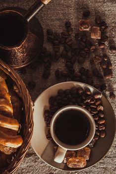 vertical A cup of coffee on textile with coffee beans, dark candy sugar, pots, basket and cake