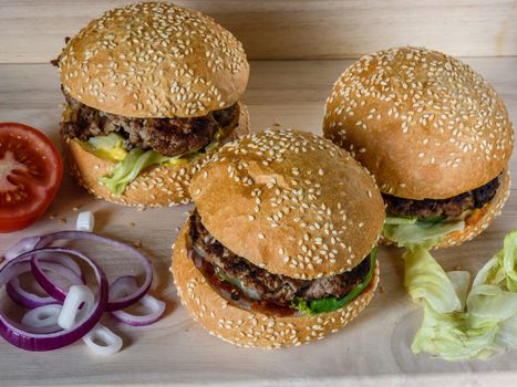 Three fresh burger lay on the board with vegetables. Homemade fast food more tasty and healthy.