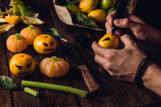 Preparation for Halloween. Young man draws a scary face on tangerines