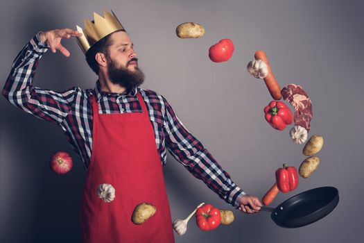 Cooking man concept, king of kitchen,bearded man in checked shirt, drop up meat and vegetables from a pan, studio shot on gray background