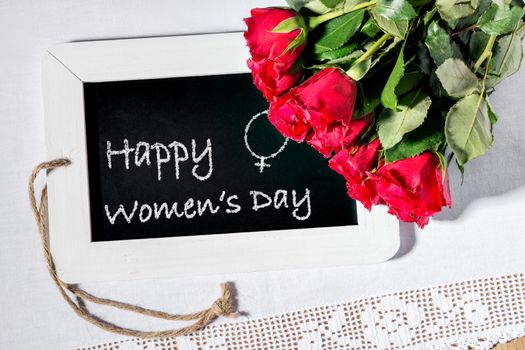 Image of a slate blackboard on a table with chalk message Happy Women's Day and women's sign and roses