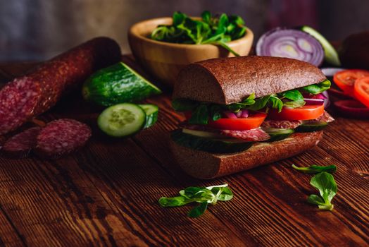 Sandwich with Salami and Fresh Vegetables on Wooden Table