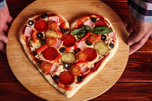 Male hands holding heart shapes pizza Valentines day surprise gift concept
