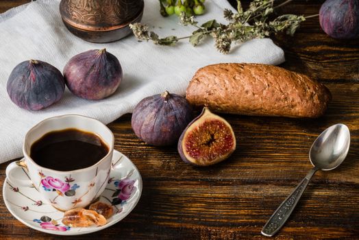 Cup of coffee with fresh bun and some figs on wooden table