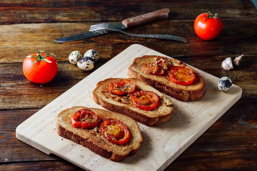 Three Toasts with Fried Tomatoes. on Cutting Board and Some Ingredients on Background