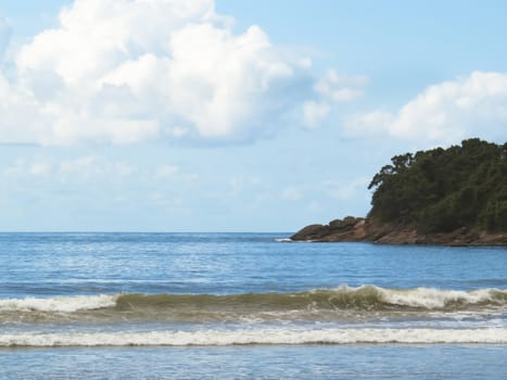 Waves on the beach with island to the background in sky with clouds.