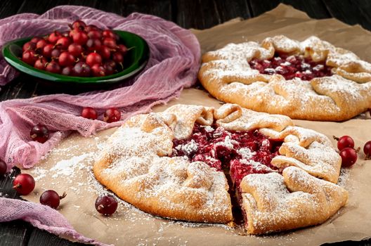 Two of gooseberry galette. Berries of gooseberry on a wooden table and in plate, decorative mesh. The cut out sector of the pie.